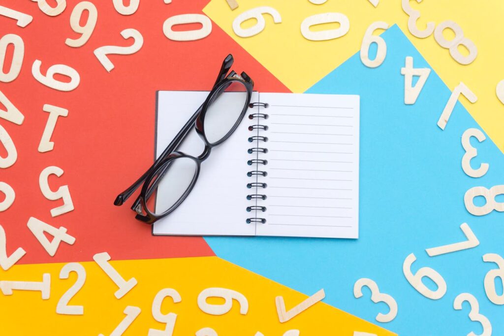 Colorful flat lay with notebook, eyeglasses, and scattered numbers on vibrant background.